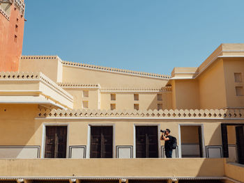 Man photographing while standing in balcony against clear sky