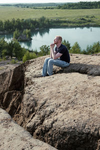 Side view of woman sitting on rock by lake