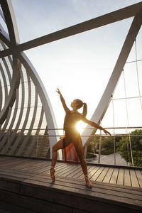 Ballerina dancing on bridge against clear sky