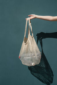 Hand of woman holding mesh bag with plastic bottles in front of wall