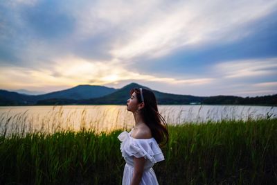 Side view of teenage girl standing on land against sky during sunset