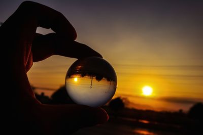 Close-up of hand holding sun against sky during sunset