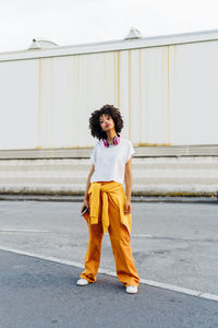 Young woman with wireless headphones standing on footpath