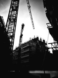 Low angle view of crane and buildings against sky