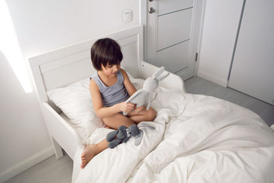 Child boy lies in a white children's bed with a blanket in a room with toys rabbits