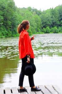 Rear view of woman standing by lake against trees