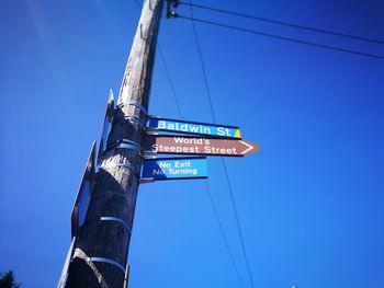 Low angle view of road sign against clear blue sky