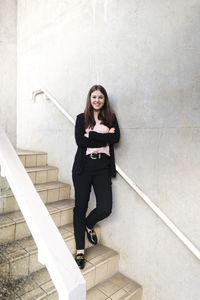 Smiling young woman with arms crossed leaning on wall