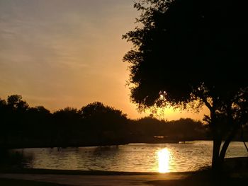 Silhouette trees by lake against sky during sunset