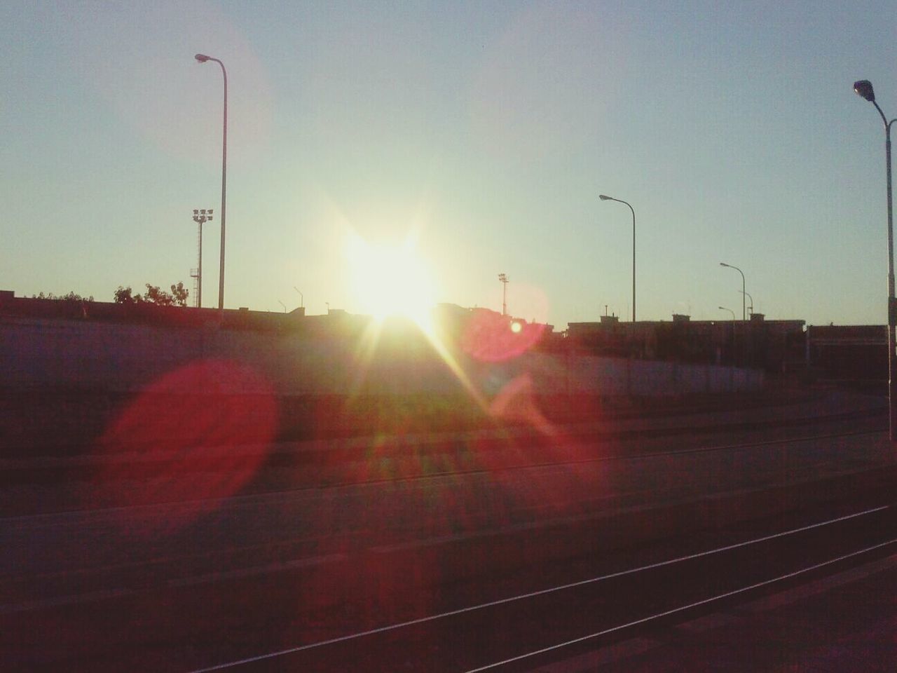 transportation, sun, lens flare, railroad track, sunset, sunbeam, sunlight, street light, sky, clear sky, rail transportation, mode of transport, public transportation, road, railroad station platform, car, outdoors, no people, travel, the way forward