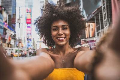 Portrait of happy young woman with afro hairstyle taking selfie on city street