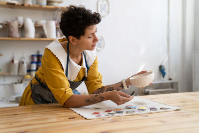 Craft crockery making, woman artist choose paint color for handmade cup in studio for online orders