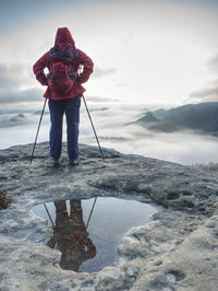 Backpack and trekking sticks at edge. woman visit dangerous viewpoint above valley with thick mist