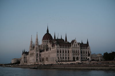 Buildings by river against clear sky