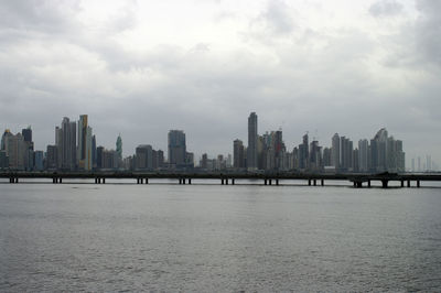 Sea by modern buildings against sky in city