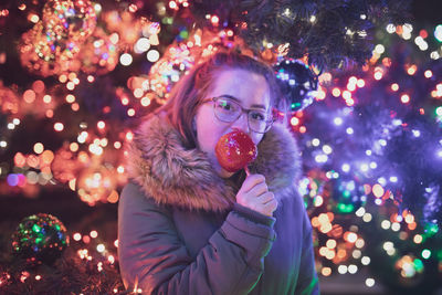 Portrait of young woman eating caramelized apple during christmas at night