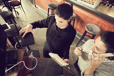 High angle view of owner holding modem while colleague talking through smart phone in cafe