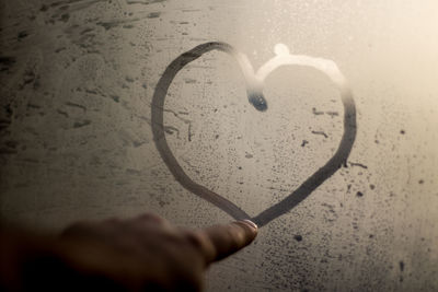 Cropped hand of person making heart shape on frosted glass