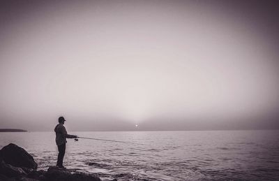 Man fishing in sea against sky