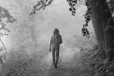 Rear view of woman walking on pathway in forest during foggy weather