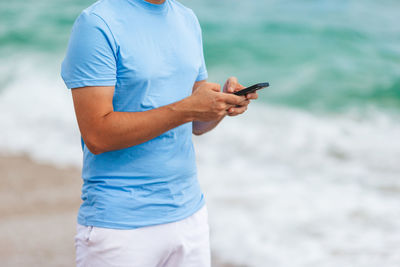 Midsection of man using mobile phone while standing outdoors