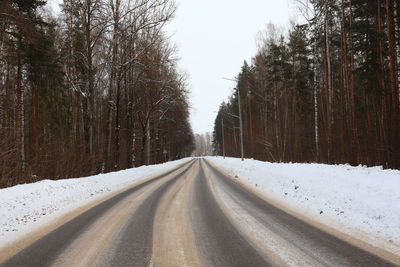 Empty road amidst snow covered trees in forest