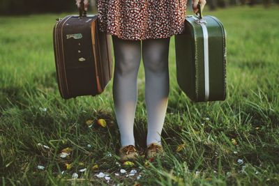 Woman in a dress and stockings holding two luggage's. concept of travel, wanderlust in a field.