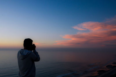 Rear view of silhouette man standing at beach during sunset