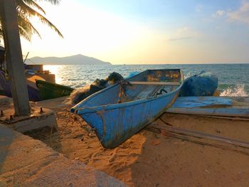 Boat moored on beach against sky during sunset