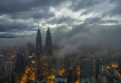 Illuminated buildings in city against cloudy sky