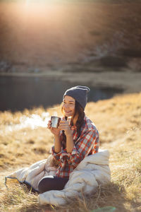 Young woman drinking coffee while sitting on land