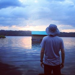 Boy standing in lake against sky during sunset