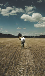 Rear view of man standing on field against sky