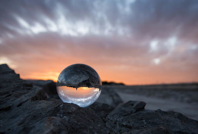 Water on rock at beach against sky during sunset