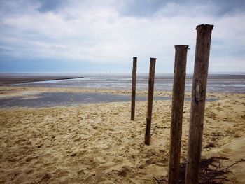 Wooden posts in sand at beach against sky