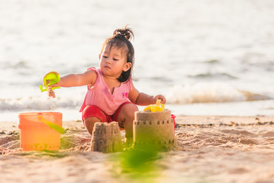 Smiling girl sitting by sandcastle on beach