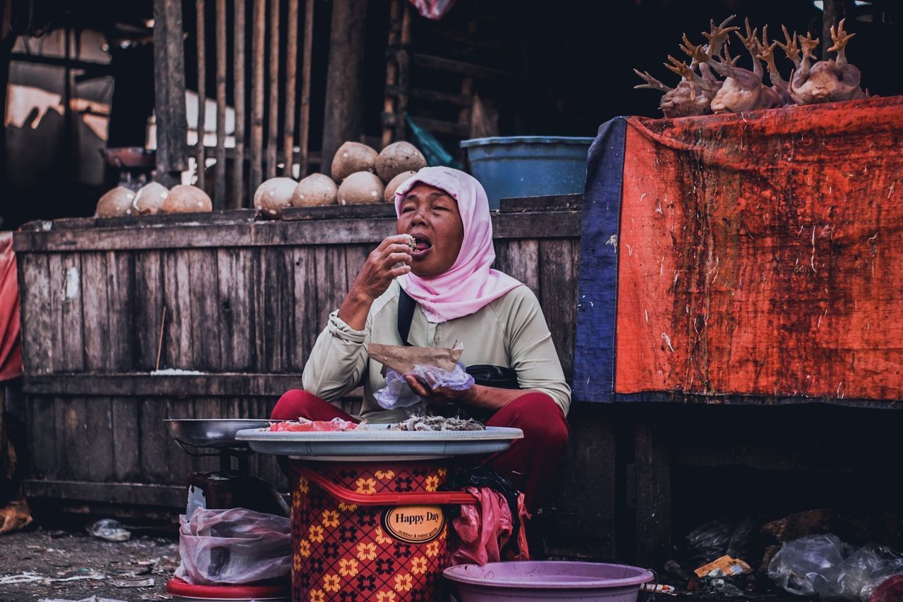 PORTRAIT OF WOMAN SITTING AT MARKET STALL