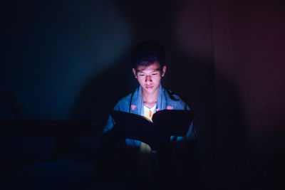 Young man reading book while sitting in darkroom at home