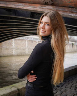 Portrait of a smiling young woman standing outdoors near river