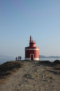 People standing by lighthouse at beach against sky