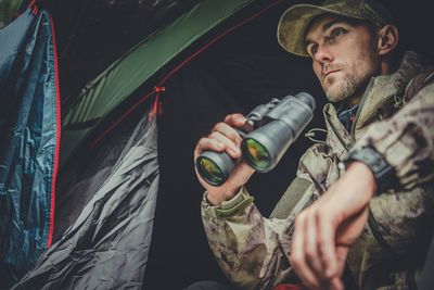 Man holding binoculars while sitting in tent