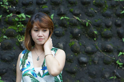 Close-up of thoughtful young woman standing against stone wall