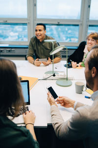 Smiling multi-ethnic business coworkers sitting at desk while discussing in board room