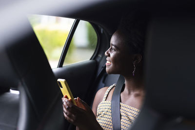 Smiling young woman with smart phone in car