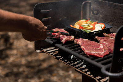 Cropped image of man preparing meat on barbeque grill at park