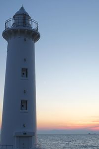 Lighthouse by sea against sky during sunset