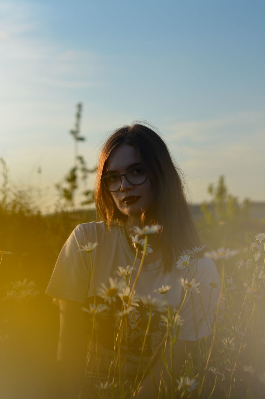 plant, one person, real people, sky, leisure activity, young adult, young women, field, lifestyles, front view, portrait, nature, looking at camera, land, hairstyle, standing, long hair, sunset, flower, hair, beautiful woman, outdoors