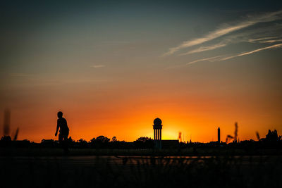 Silhouette man standing against orange sky during sunset