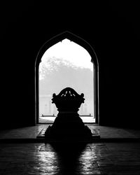 Silhouette of a tomb on floor against sky seen through door