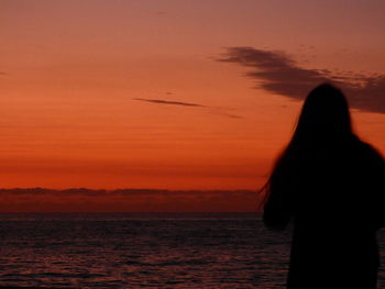 Silhouette woman flying over sea against sky during sunset